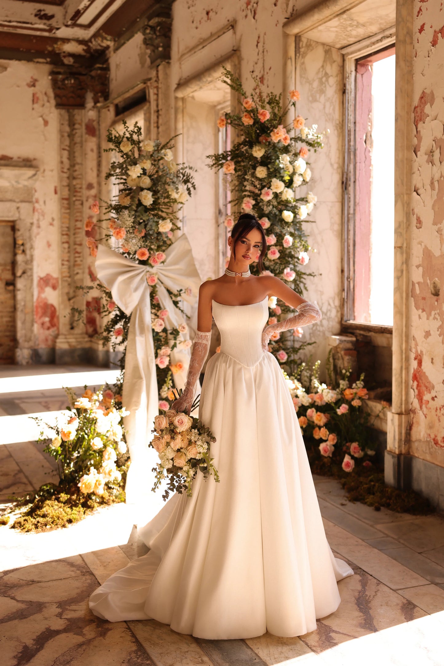 Bride in elegant satin wedding gown with flowing train and floral arch backdrop