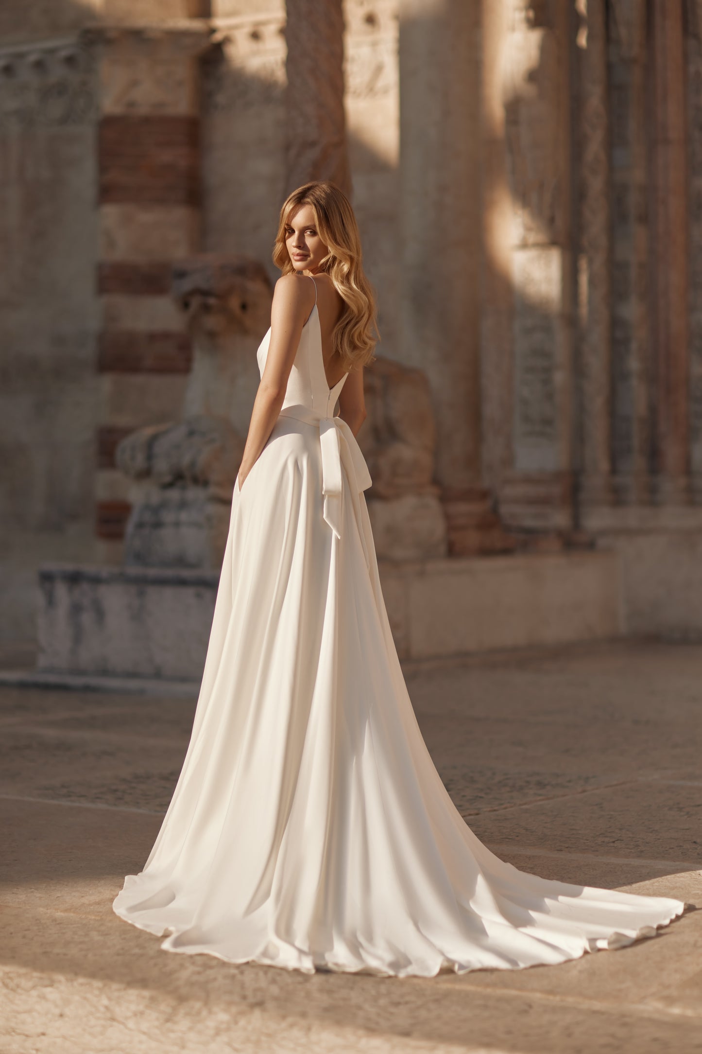 Woman in a white wedding dress standing in front of an ancient stone building.