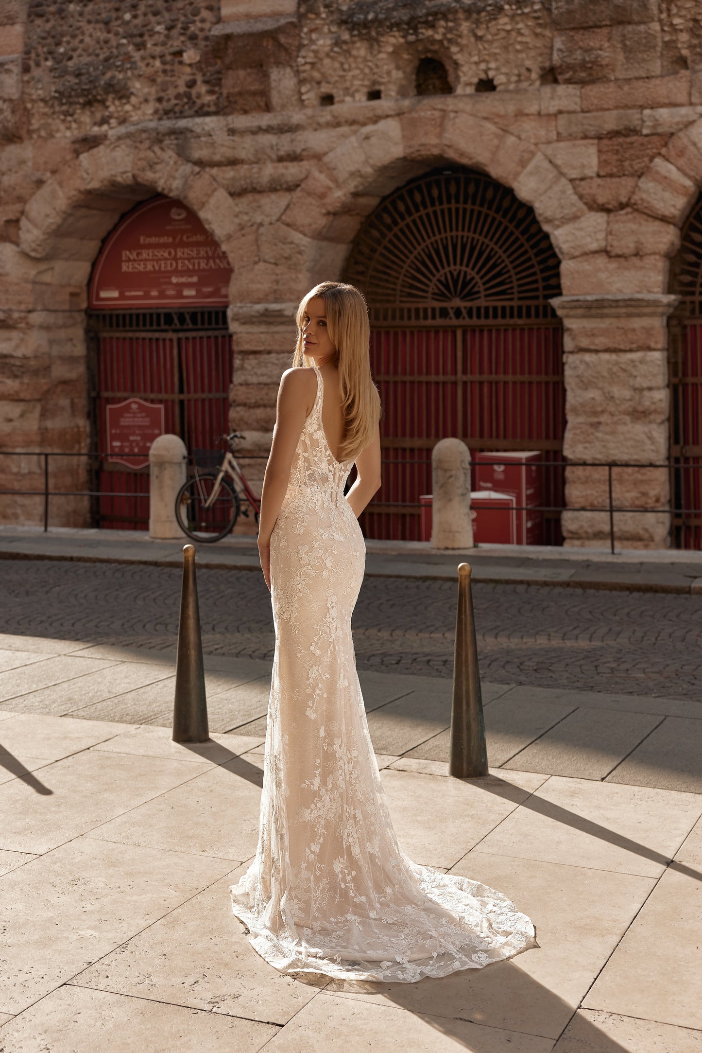 Woman in a white lace wedding dress standing in front of an ancient stone building.