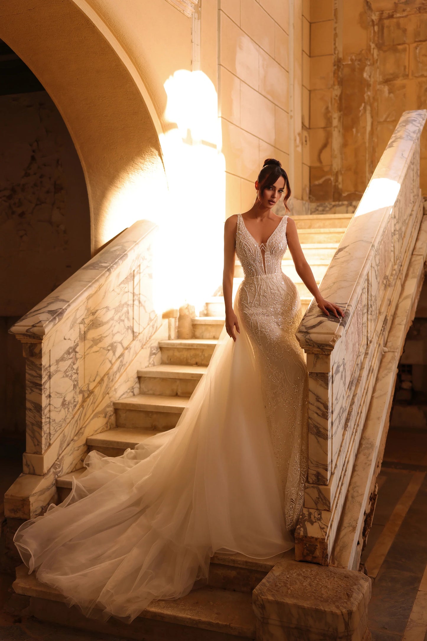Bride on staircase in gown with flowing tulle overlay and plunging neckline