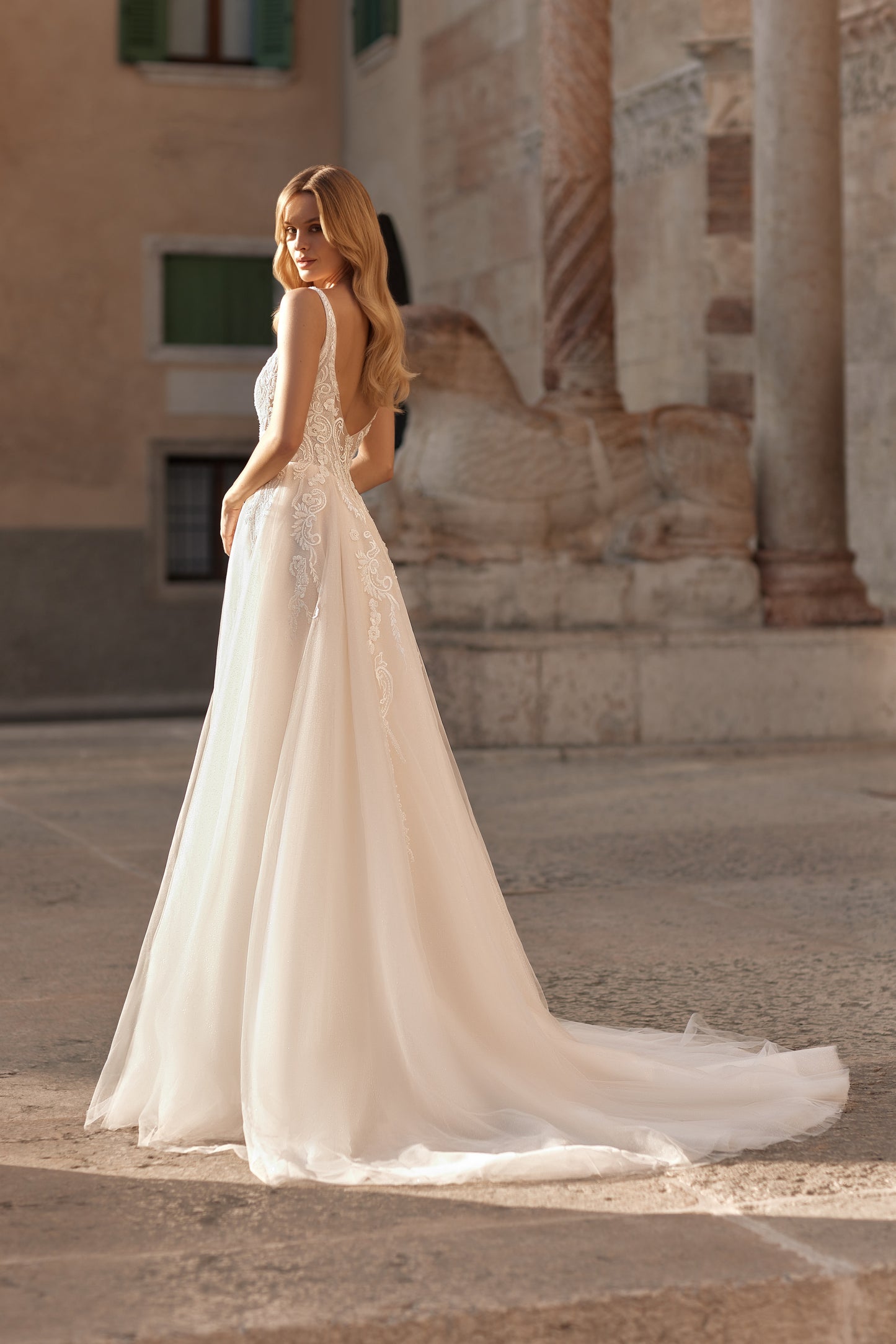Woman in a white wedding dress standing in an outdoor setting with classical architecture.