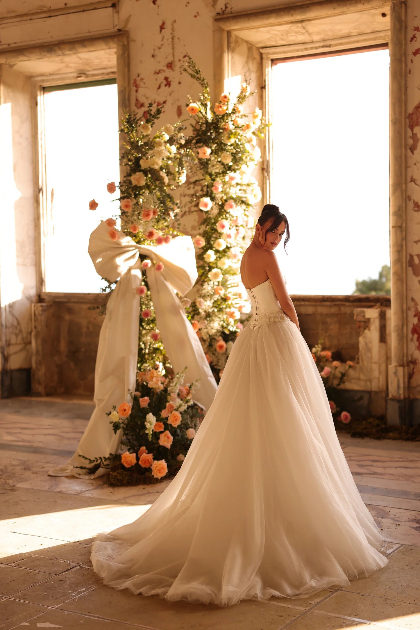 Full view of the Flory gown showing the lace-up back and flowing silhouette in an elegant indoor setting.