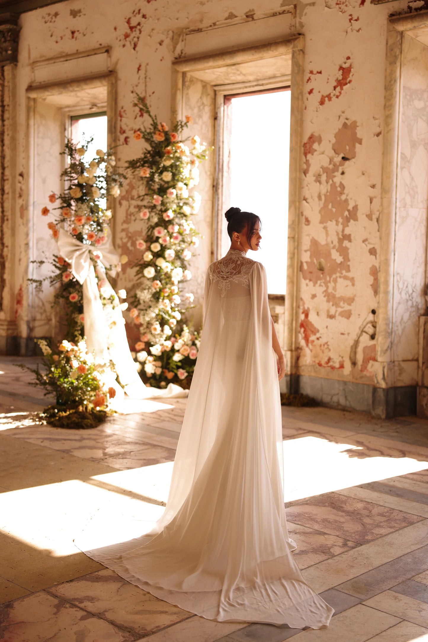 Elegant bridal gown with detachable cape and sunlight streaming in