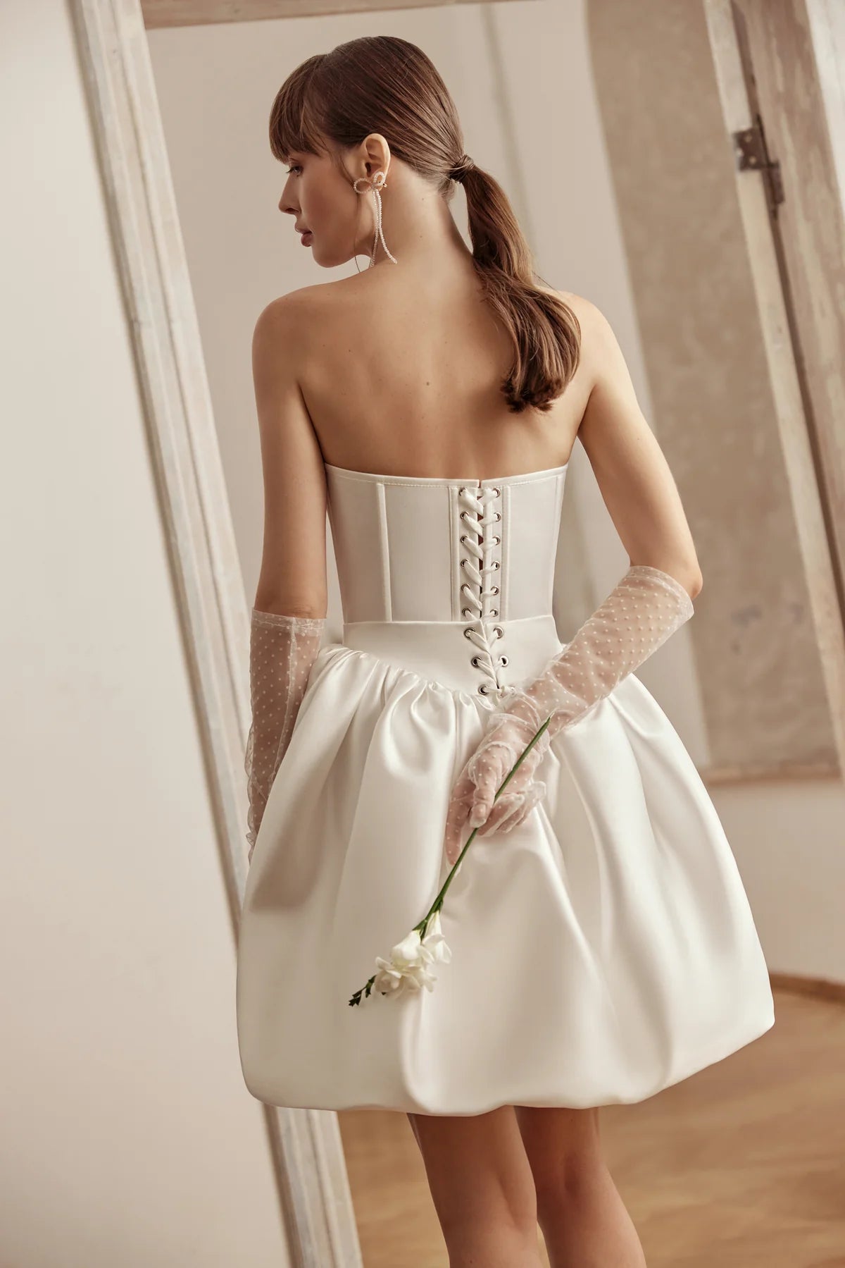 Bride in an ivory satin mini dress featuring a voluminous skirt, sweetheart neckline, and structured bodice, posing gracefully.