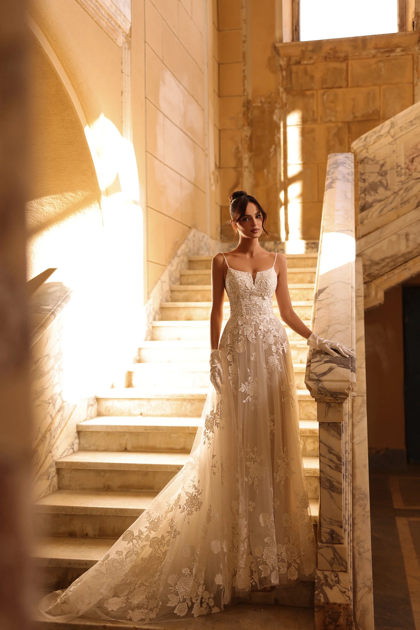 Bride in lace wedding dress walking down a stone staircase, sunlight behind.