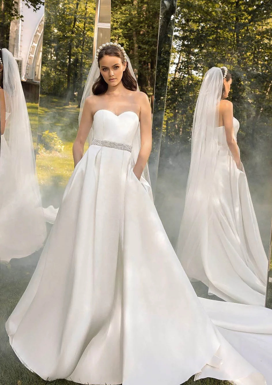 Bride in a princess gown with pearl-embroidered bodice and flowing satin skirt, posing outdoors with a veil.