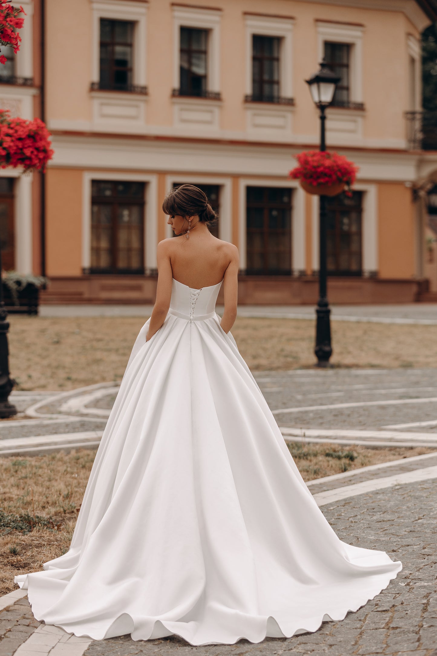 Bride holding A-line gown, featuring pleated bodice and lace-up back