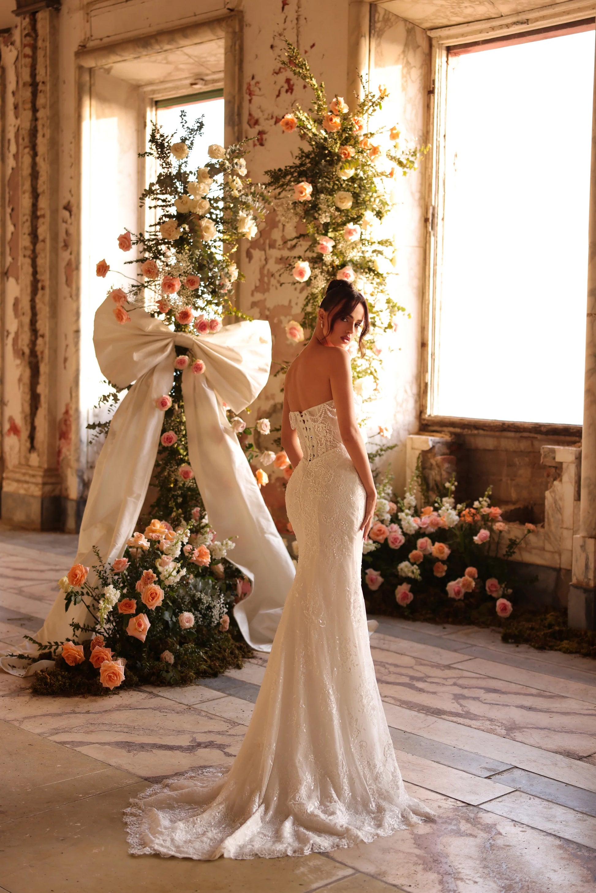 Sweeping train and open back framed by floral arch in soft light