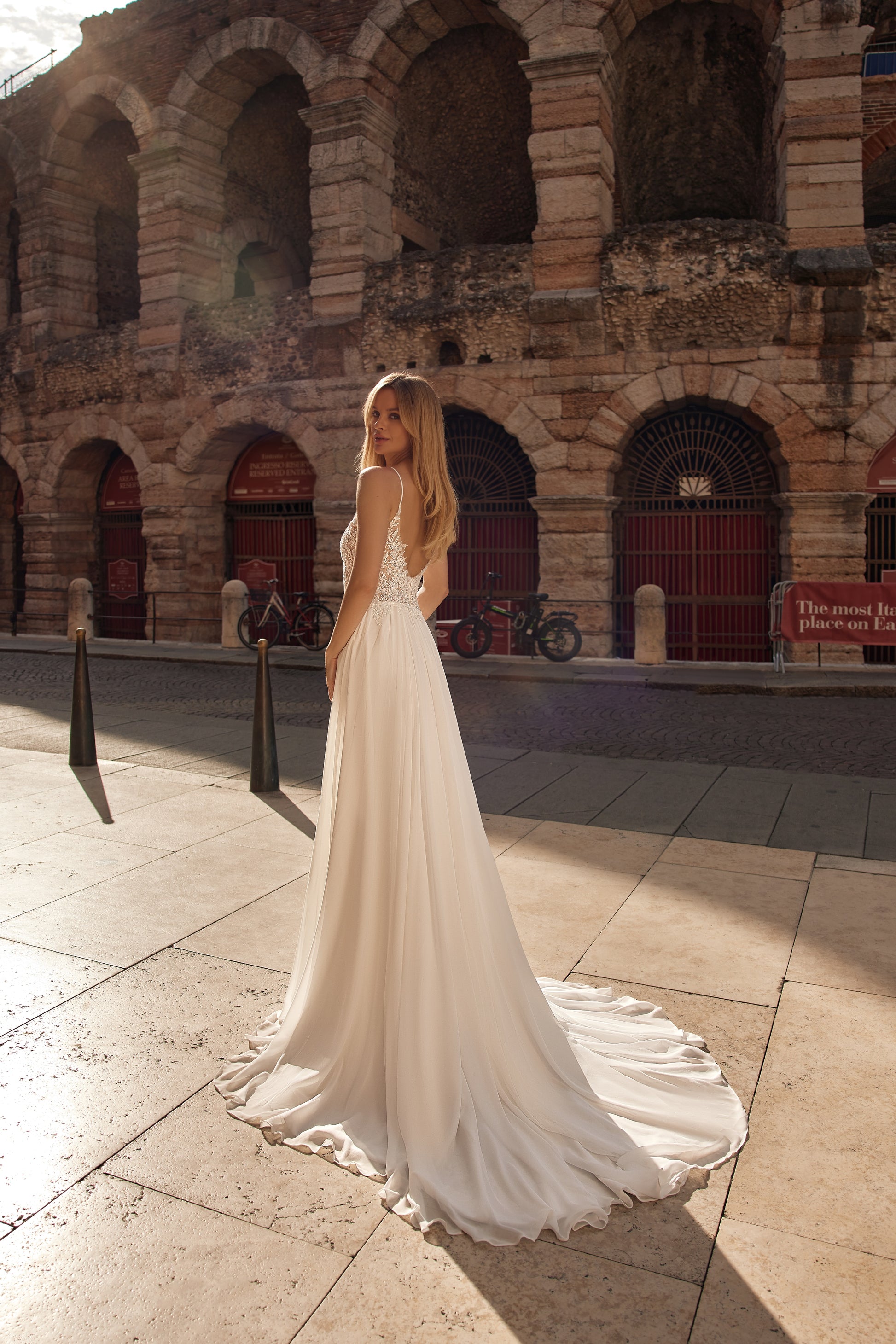 Woman in a white wedding dress standing in front of an ancient amphitheater.