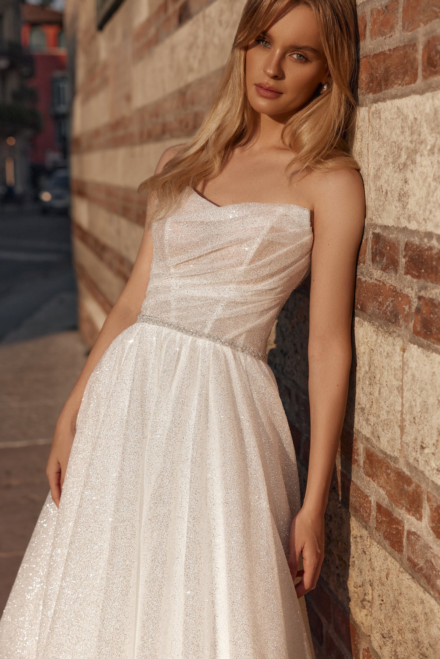 Woman in a white strapless dress leaning against a brick wall.