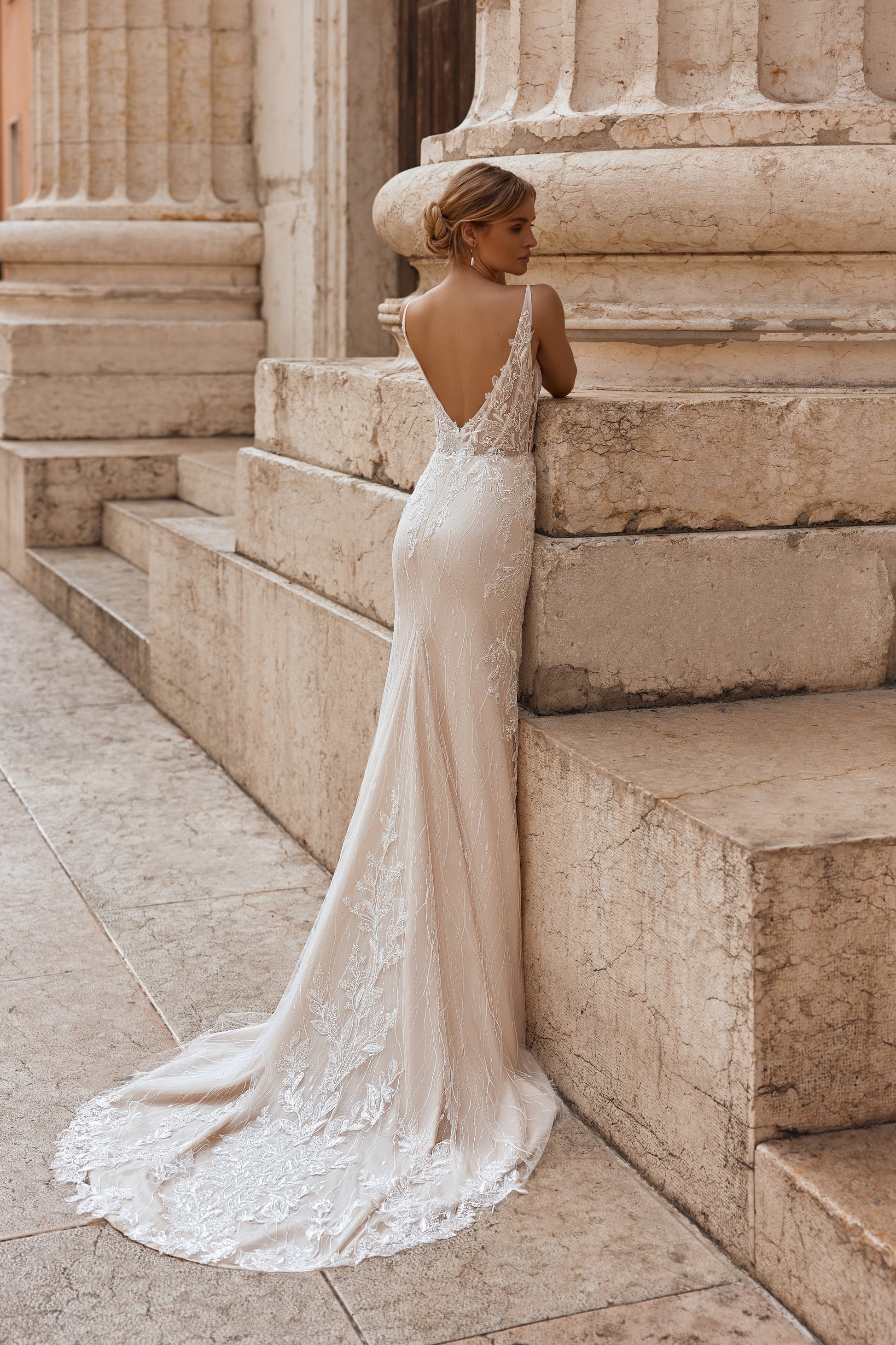 Woman in a white lace wedding dress standing on stone steps.