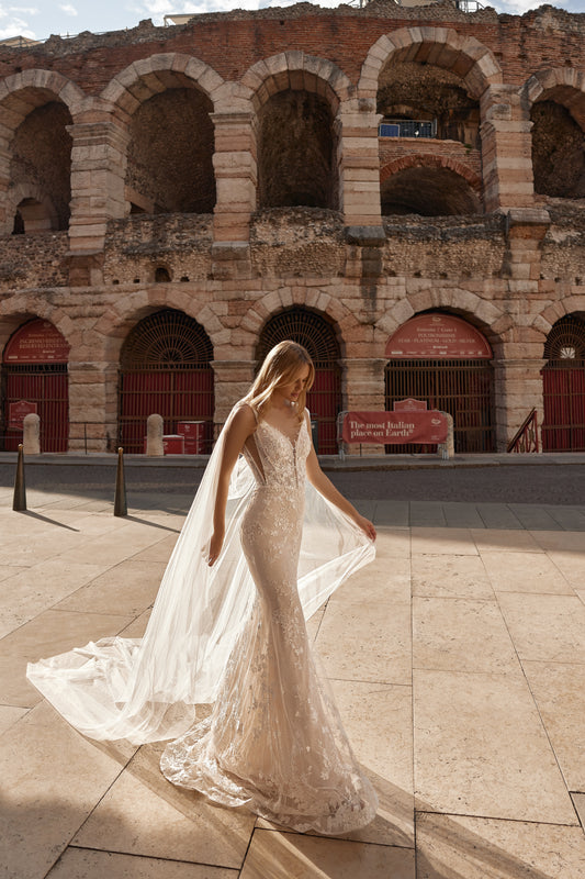 Bride in nude-toned gown with 3D floral lace, sheer tulle cape, and soft train