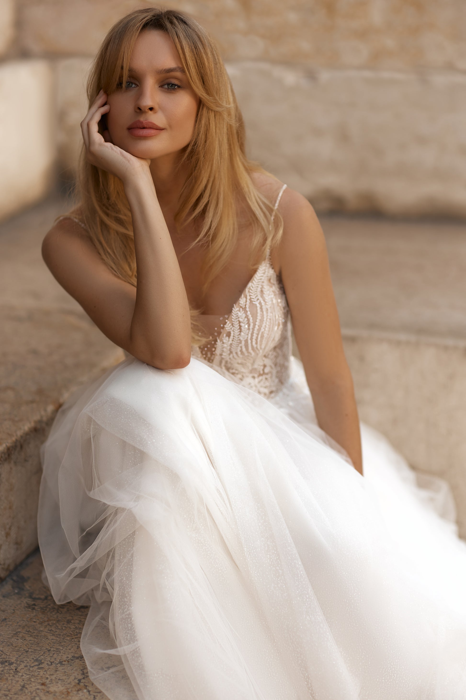 Woman in a white wedding dress sitting on stone steps.