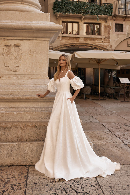 Bride in ivory wedding gown with embossed fabric, open back, and long flowing sleeves