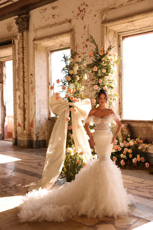 Bride in sparkling fitted gown with off-shoulder feathered sleeves and ruffled train