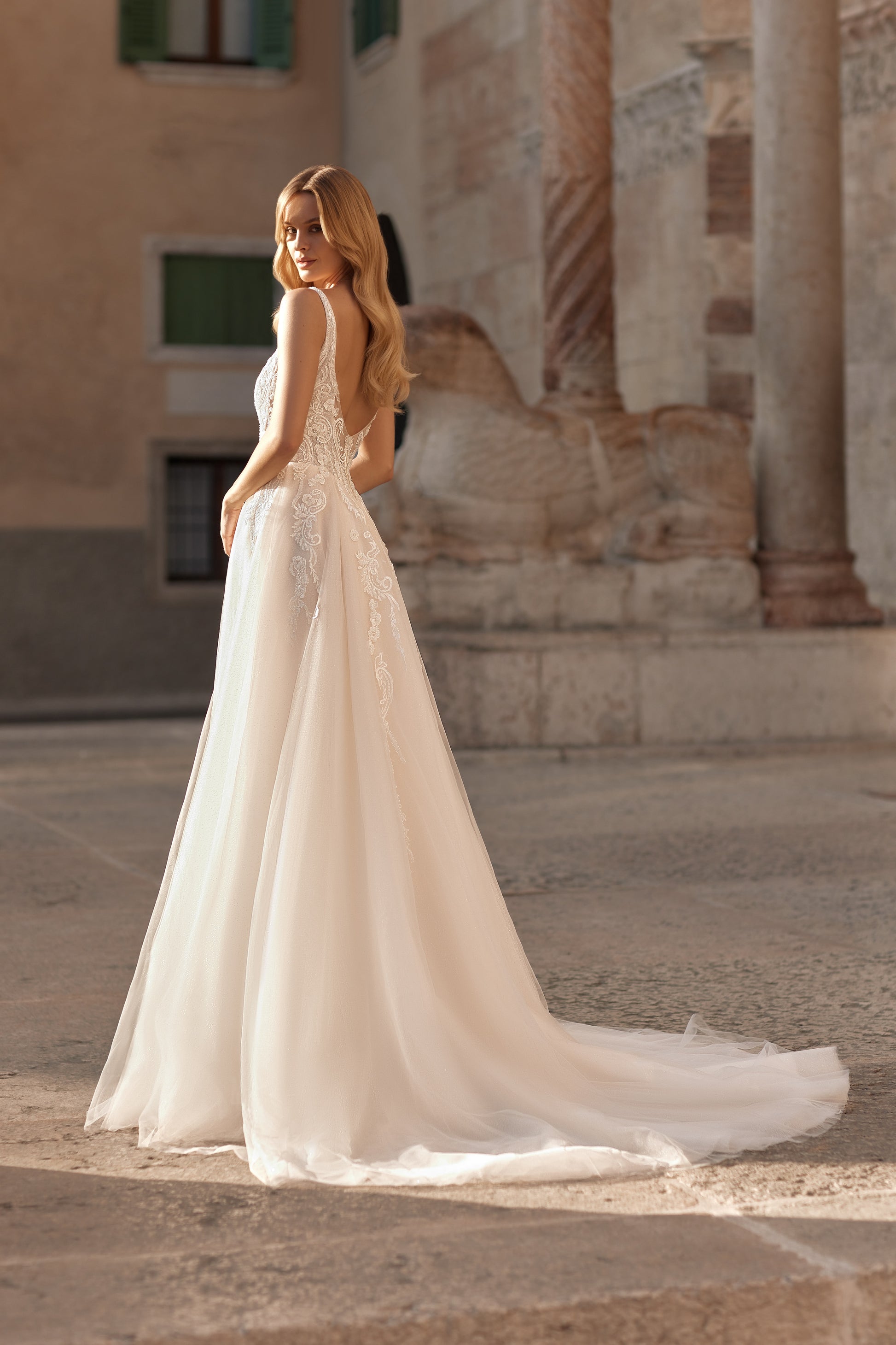 Woman in a white wedding dress standing in an outdoor setting with classical architecture.
