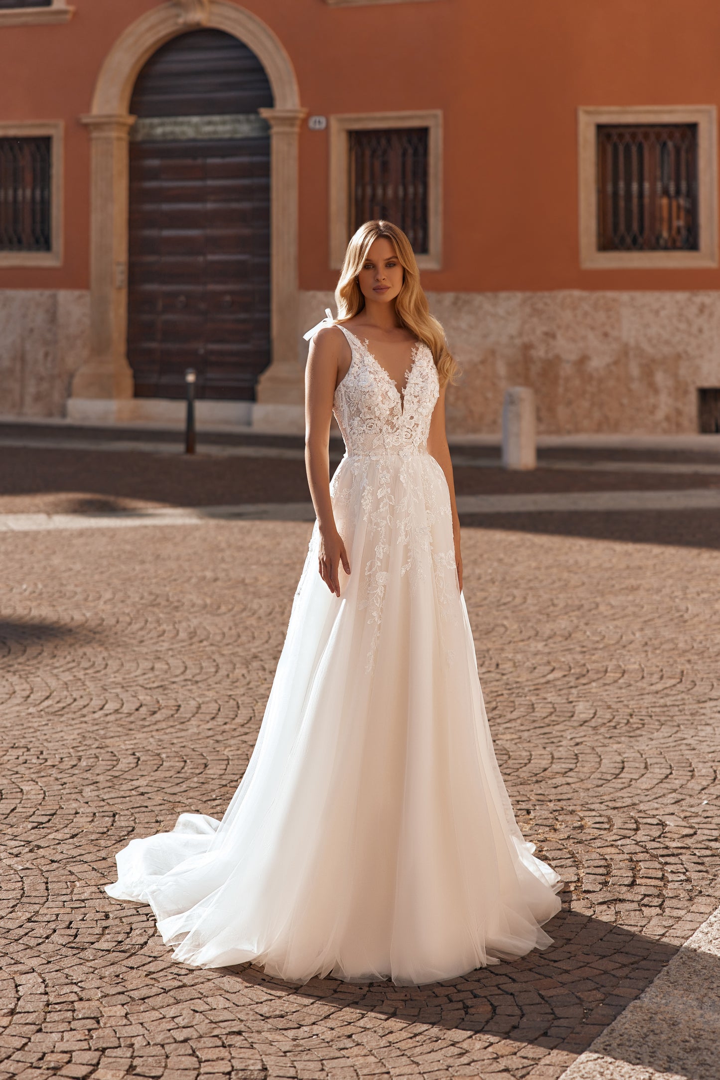 Bride in fitted lace wedding gown with delicate straps, floral details, and a long flowing tulle skirt