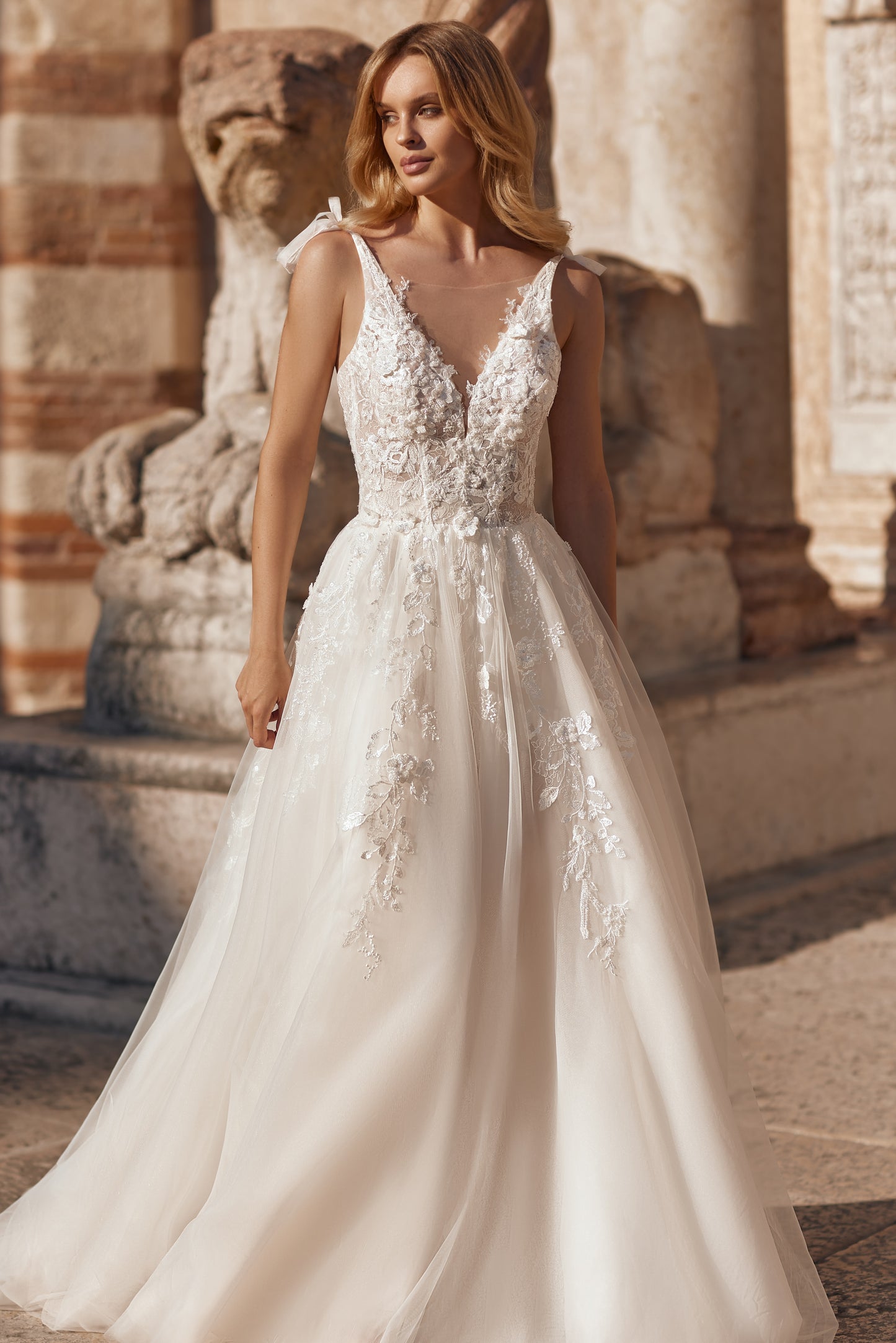 Woman in a white wedding dress standing in front of stone architectural elements.