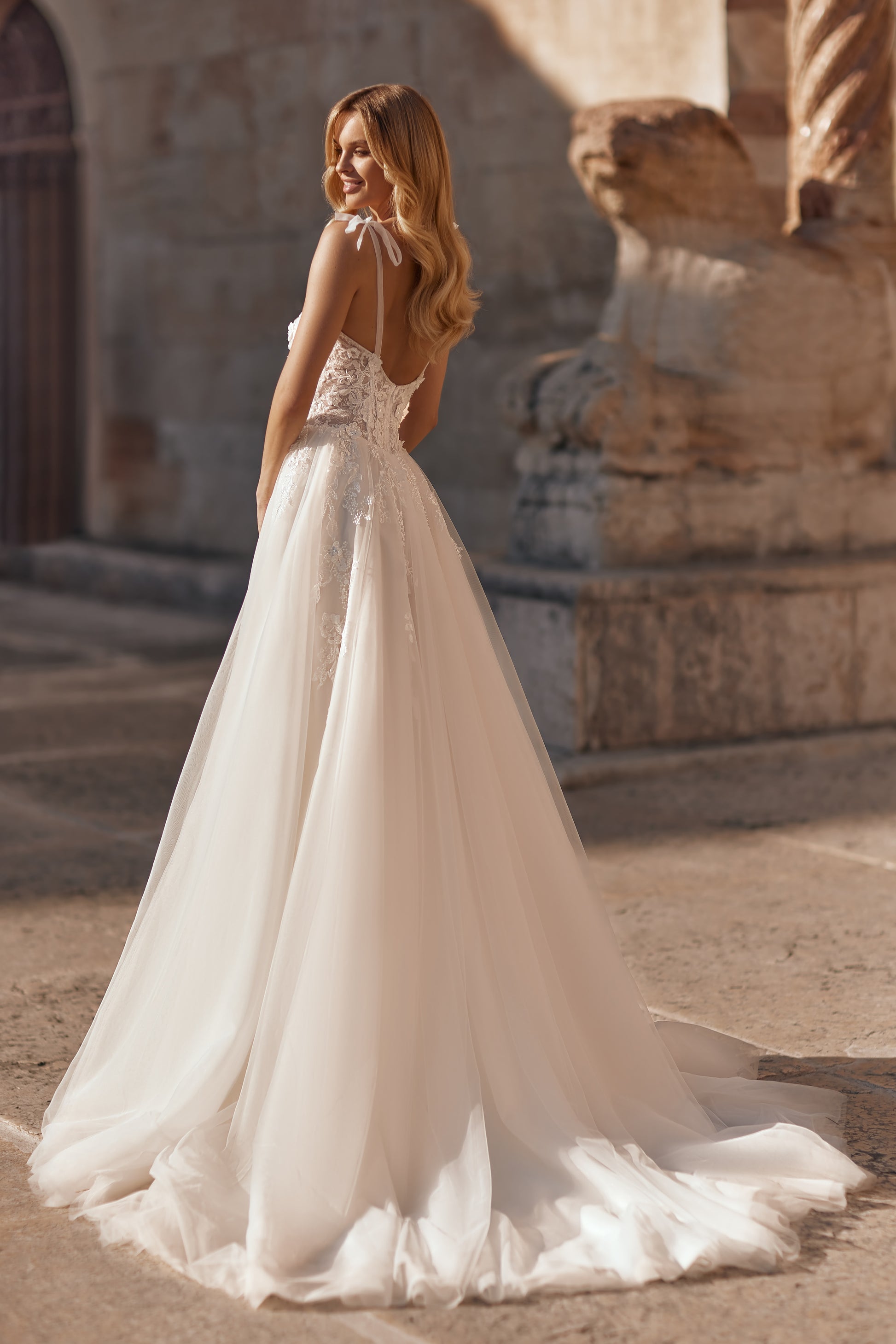 Elegant wedding gown with floral lace bodice, delicate bows on shoulders, and long train