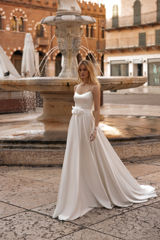 Bride in ivory gown with delicate straps and flowy train, standing near fountain