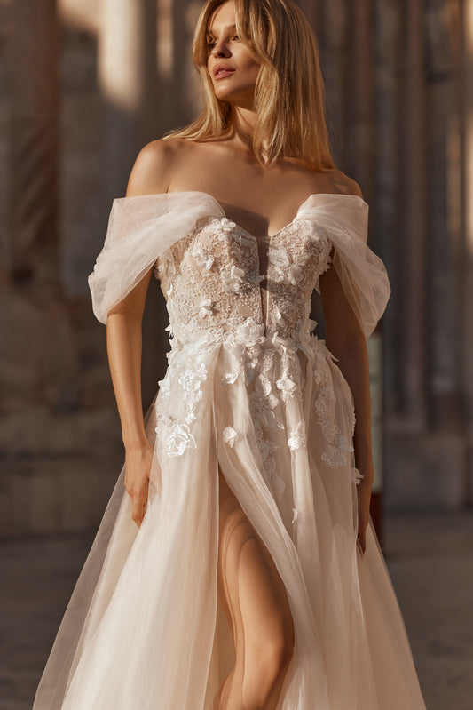 Bride in peach wedding gown with floral corset and voluminous skirt, off-shoulder sleeves