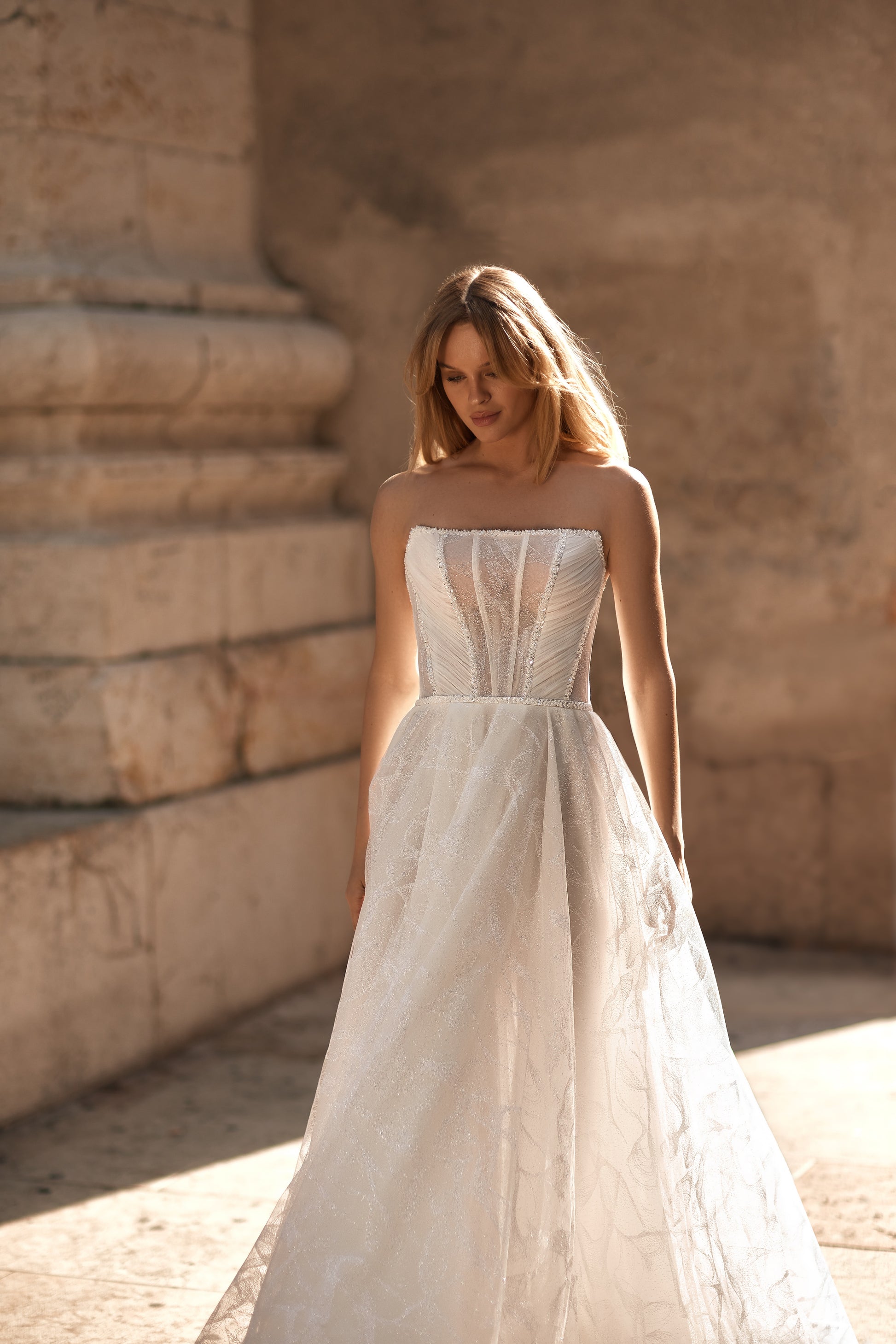 Woman in a strapless wedding dress standing against a stone wall.
