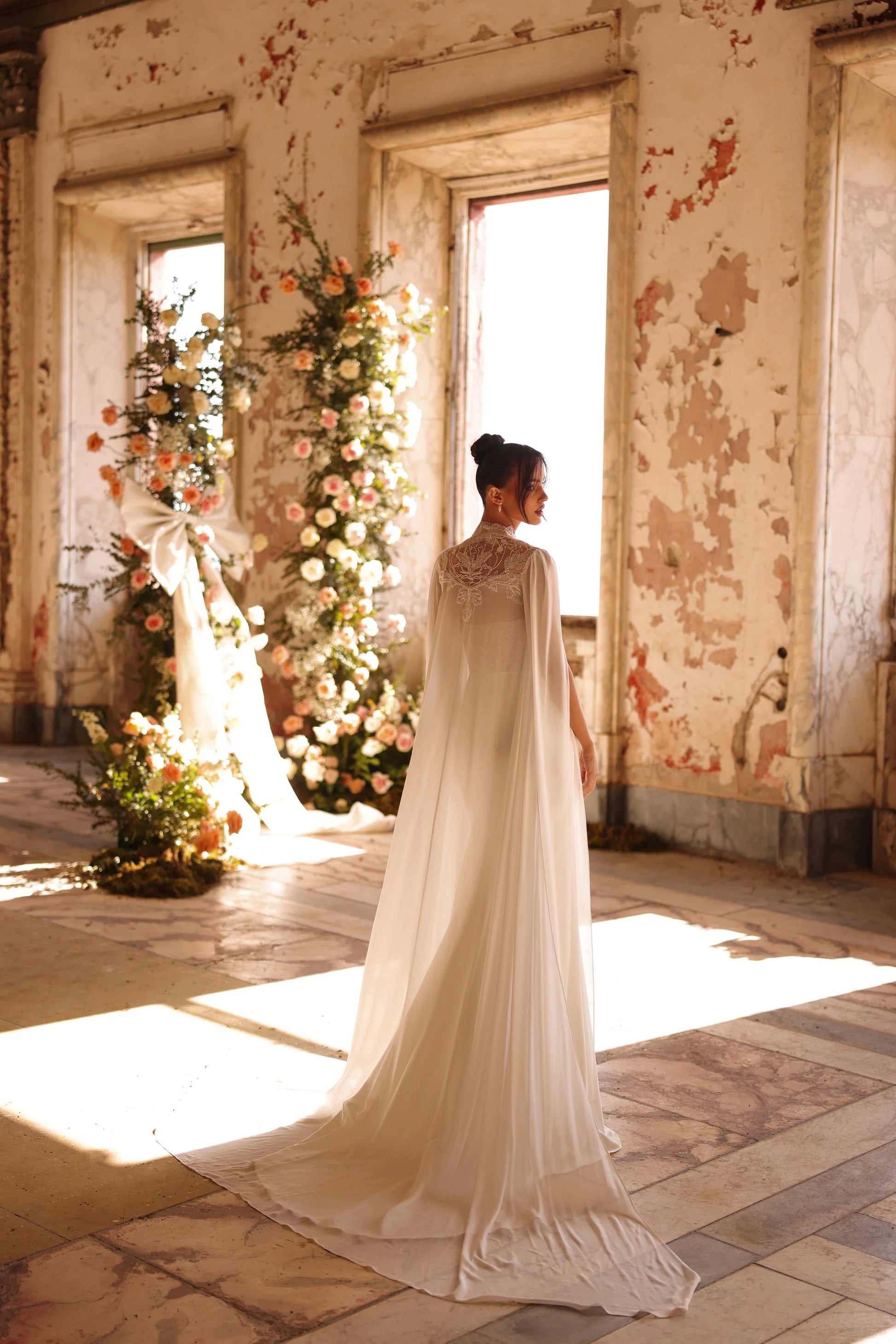 Elegant bridal gown with detachable cape and sunlight streaming in