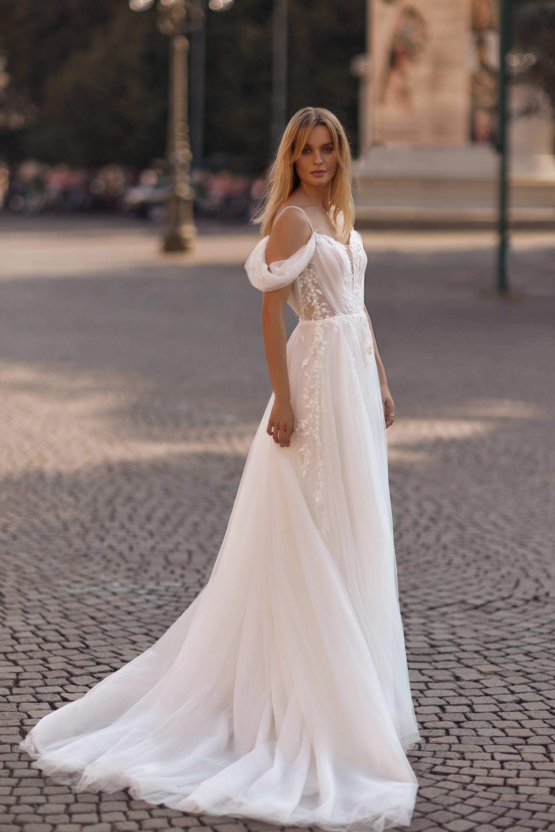 Woman in a white wedding dress standing on a cobblestone street.
