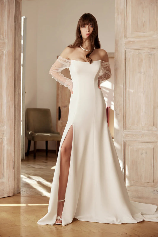 Bride in an elegant ivory satin wedding gown with a slim silhouette, side slit, and sheer embellished sleeves.