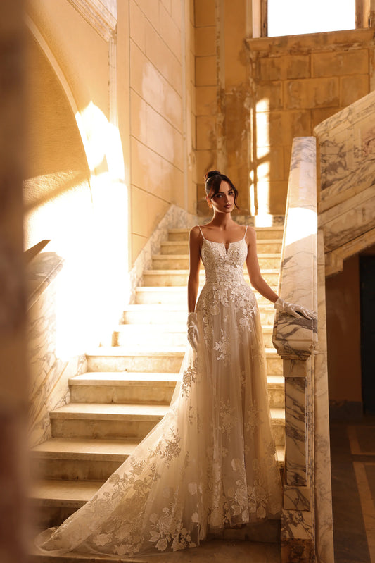 Bride in lace wedding dress walking down a stone staircase, sunlight behind.