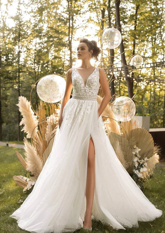 Bride wearing a lace A-line wedding dress with a high slit, standing outdoors surrounded by pampas grass and warm golden light.
